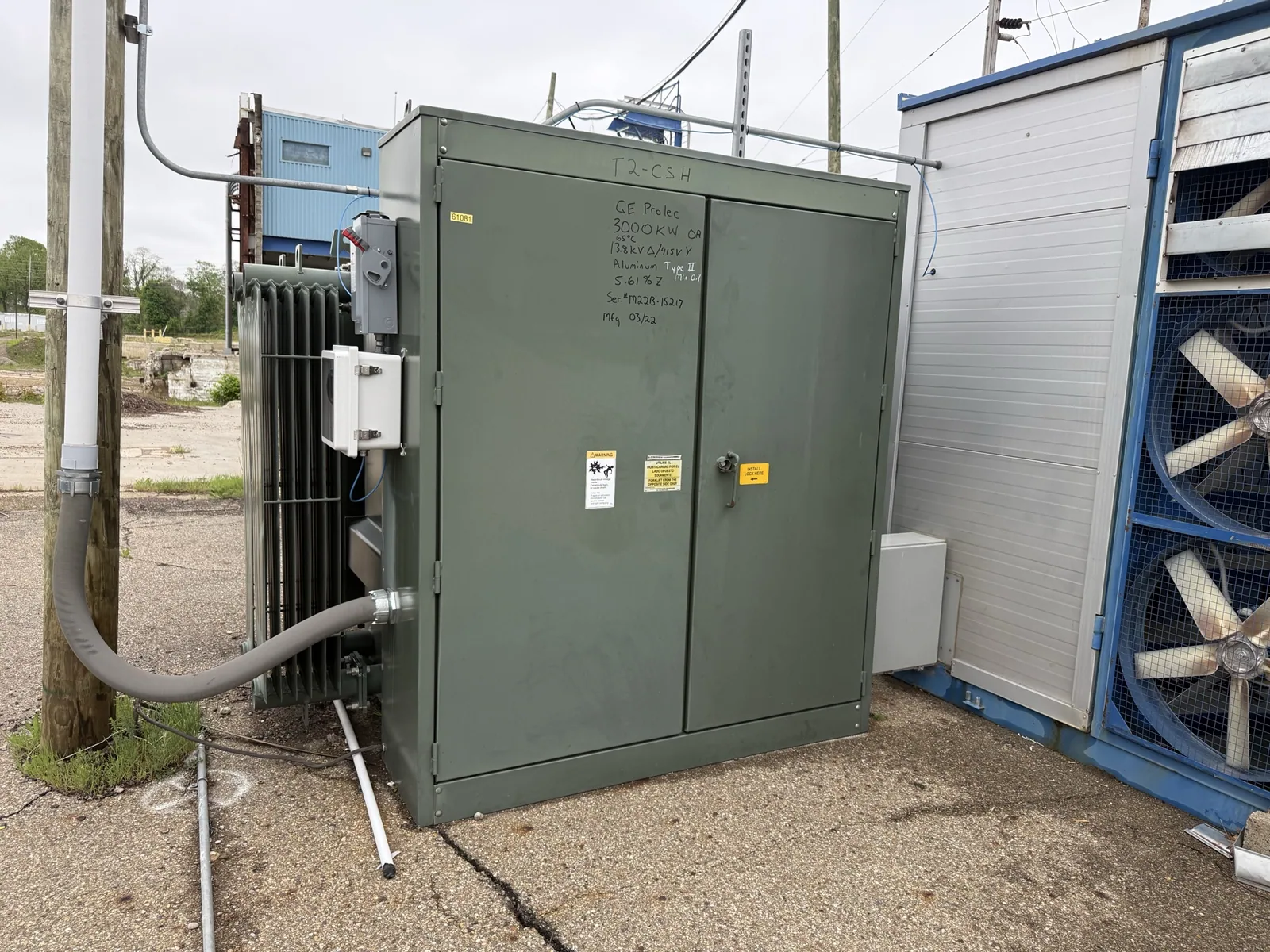 Green pad-mount transformer with radiator fins beside a plant building — Bellview, FL